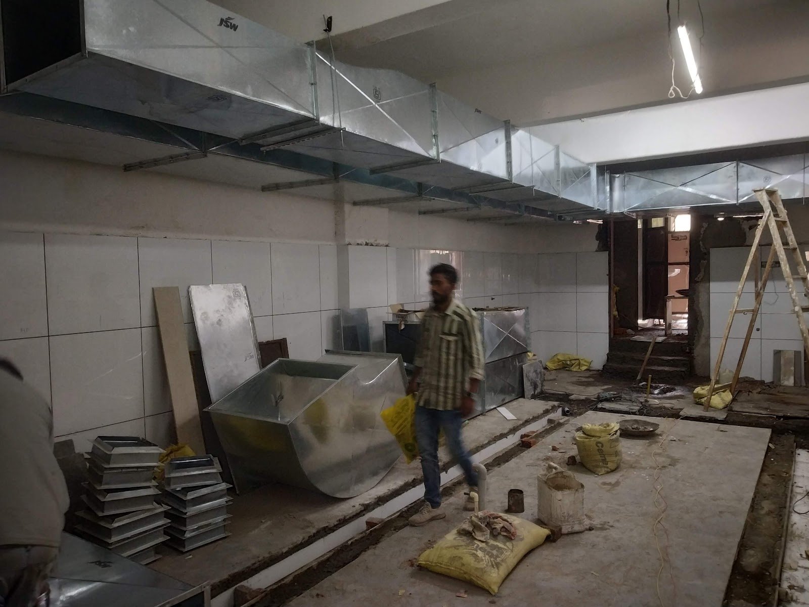 Commercial kitchen under construction with ducting overhead and a worker on site