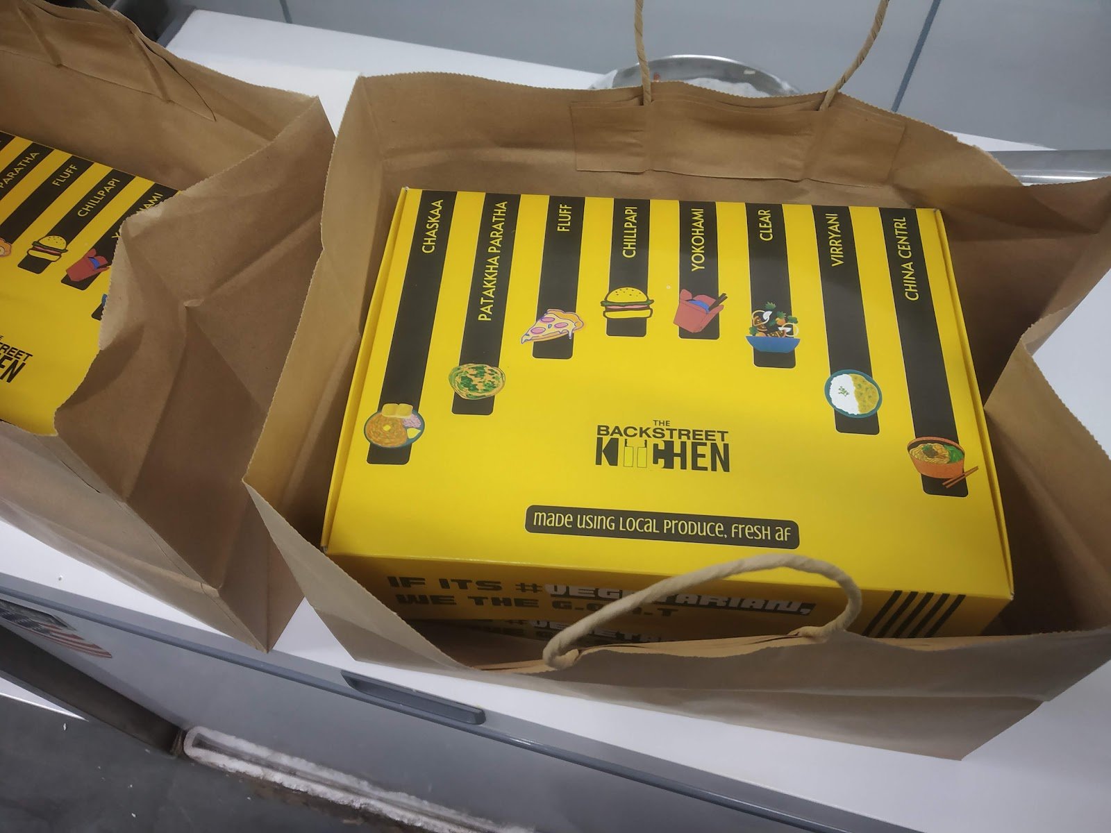 Yellow Backstreet Kitchens delivery box packed inside a paper carry bag