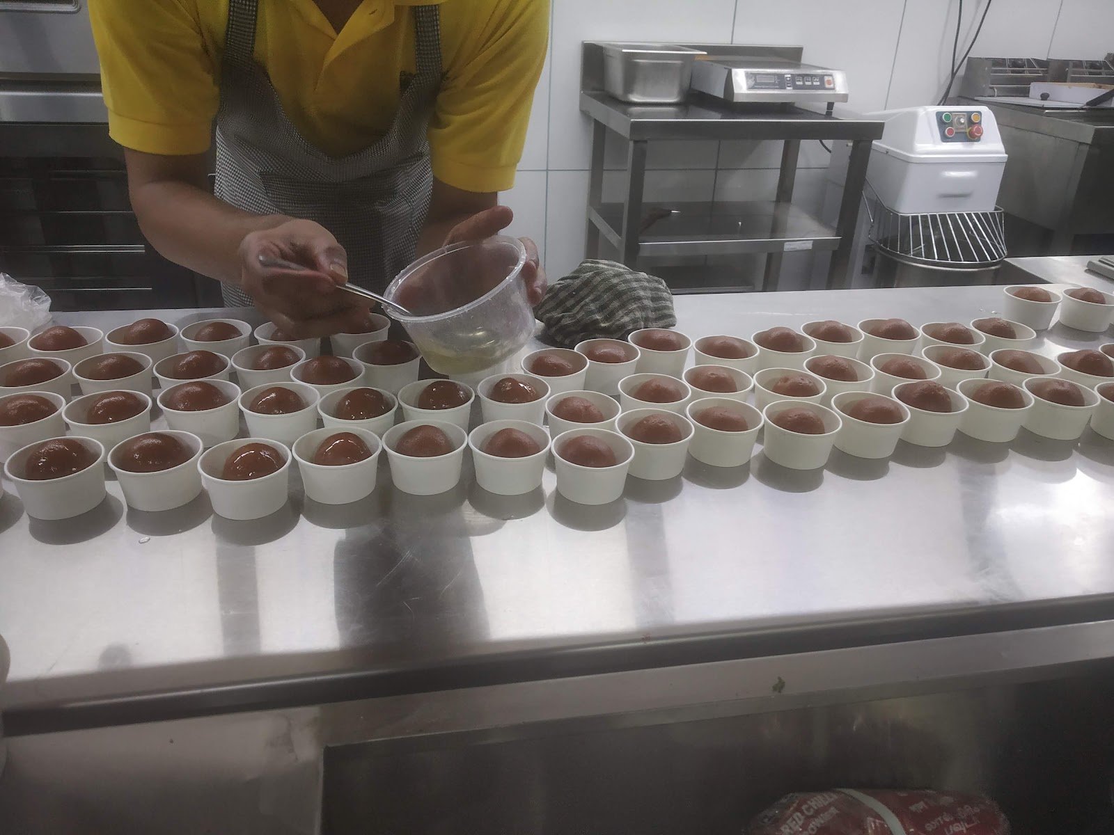 Kitchen team portioning dishes into rows of small bowls on a steel counter