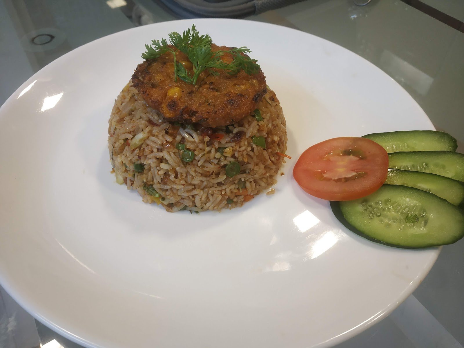 Plated seasoned rice with a golden cutlet, tomato slices and cucumber
