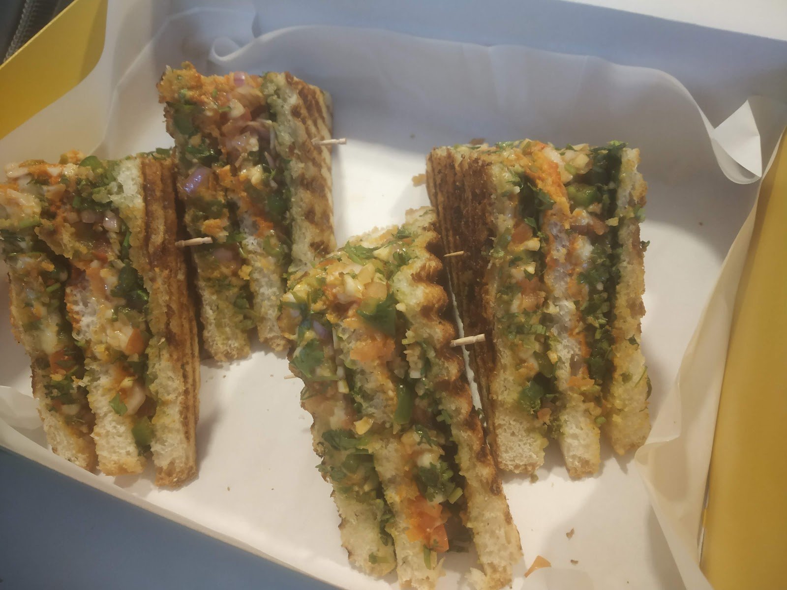 Grilled sandwiches layered with green chutney and fillings on a white plate