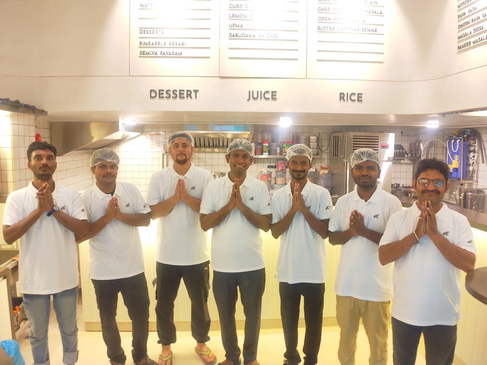 The Madras Canteens team in white uniforms and hair caps standing together with folded hands